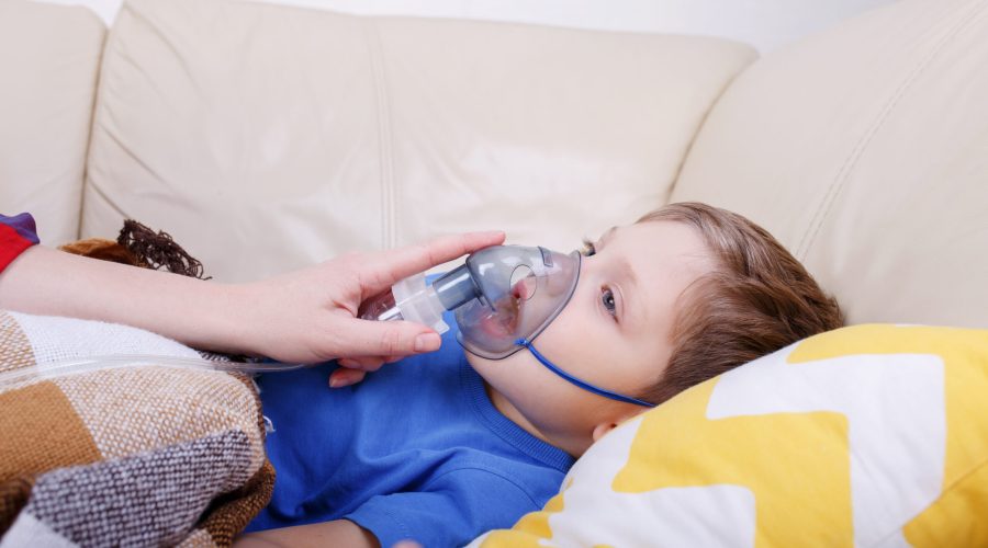 Mother holds a nebulizer mask in the boy's face during inhalation. Sick chid with pediatric nebulizer. Little kid with asthma or bronchitis has trouble breathing.